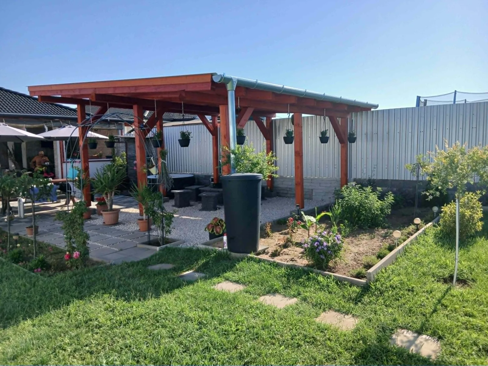 Elkészült lakkozott fa pergola és kerti terasz kaviccsal, virágokkal