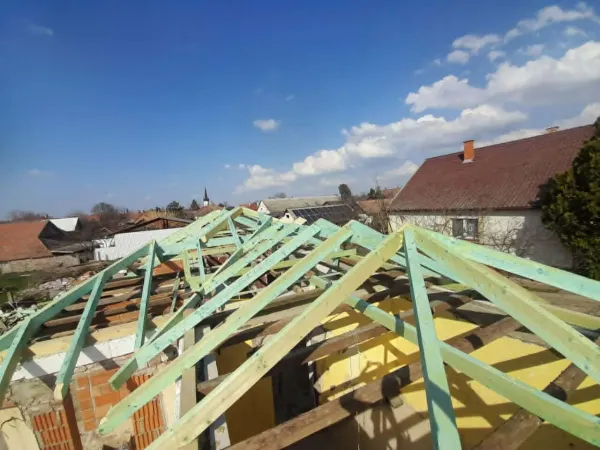 Tetőfelújítás új kontyolt fa szerkezettel, háttérben falu