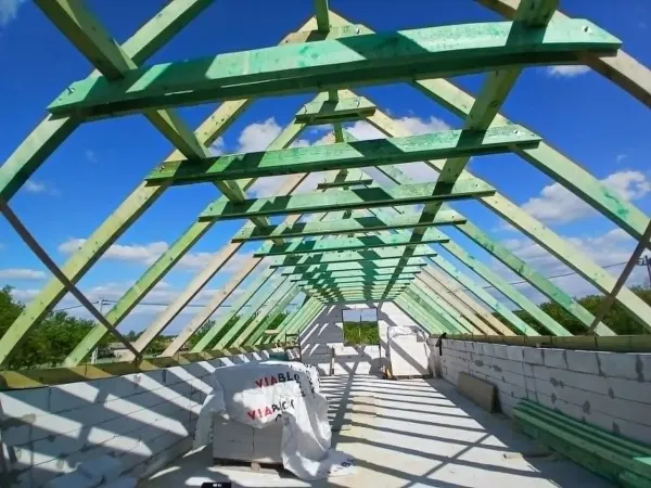 Hosszú fa tetőszerkezet belülről, zöld gerendák és a kék ég