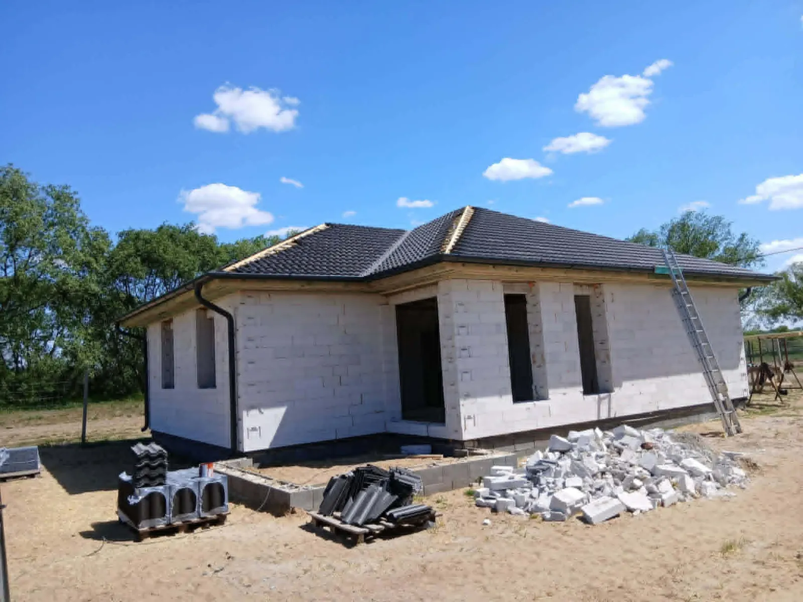Elkészült kontyolt tető sötét antracit betoncseréppel, napos kék ég